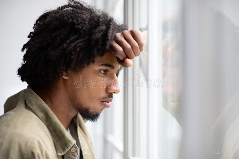 Depressionsbegrepp. Bild av en bitter, upprörd ung svart man som tittar ut genom fönstret arkivfoto