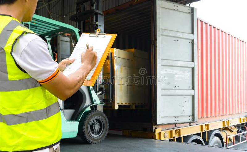 Depósito de trabalhador segurando pranchetas controle empilhador carregando mercadorias de remessa no caminhão de contêiner. fotografia de stock Depósito de trabalhador segurando pranchetas controle empilhador carregando mercadorias de remessa no caminhão de contêiner. fotografia de stock