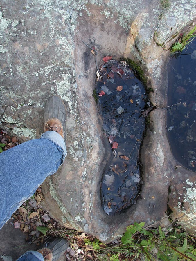 A huge footprint in stone next to a human's foot. A huge footprint in stone next to a human's foot.