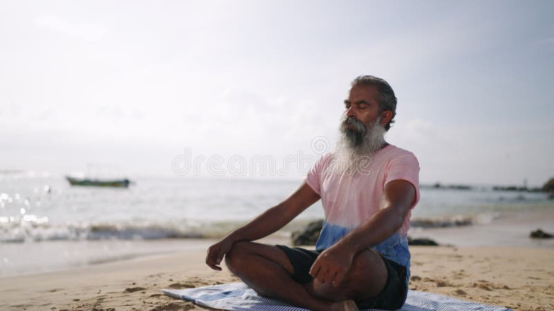 Der alte Mann, der meditiert und in Lotus sitzt, strahlt Wellen am paradiesischen Inselstrand am Ozean aus. schwarzes Männchen stock video