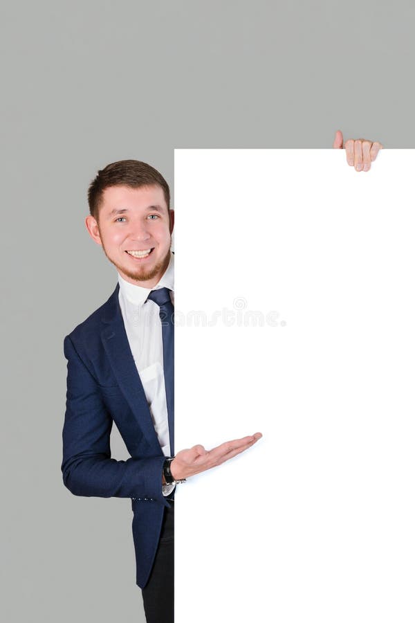 Der Geschäftsmann zeigt mit seiner Handfläche auf das weiße leere Brett auf grauem Hintergrund stockbilder