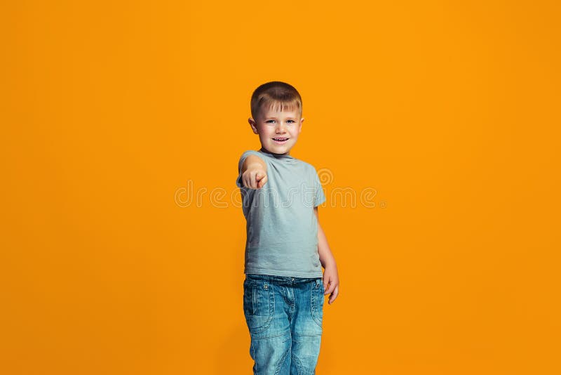 Der glückliche jugendlich Junge, der auf Sie, halbes Längennahaufnahmeporträt auf orange Hintergrund zeigt lizenzfreie stockfotos Der glückliche jugendlich Junge, der auf Sie, halbes Längennahaufnahmeporträt auf orange Hintergrund zeigt lizenzfreie stockfotos