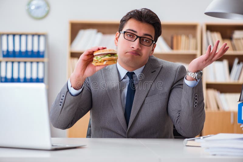 Der hungrige lustige Geschäftsmann, der Sandwich der ungesunden Fertigkost isst