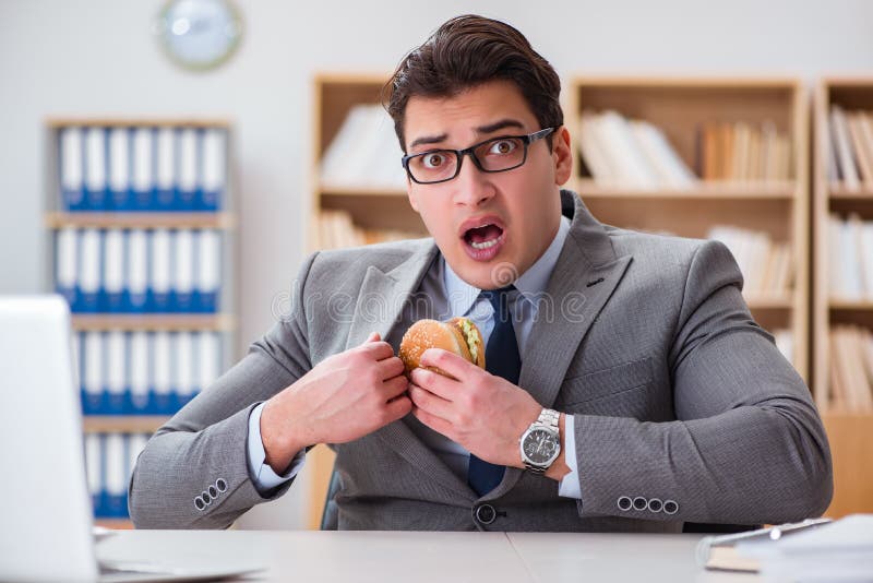 Der hungrige lustige Geschäftsmann, der Sandwich der ungesunden Fertigkost isst
