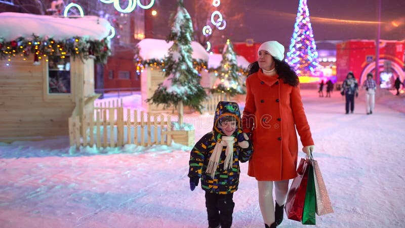 Der Junge hält eine Hand von der Mutter Elternteil hält Pakete mit Weihnachtsgeschenken Familien-Weihnachtseinkaufen Der Junge de