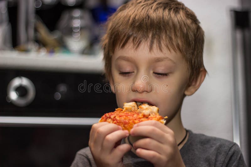 Der Junge isst eine sehr geschmackvolle Pizza mit großem Vergnügen stockbild Der Junge isst eine sehr geschmackvolle Pizza mit großem Vergnügen stockbild