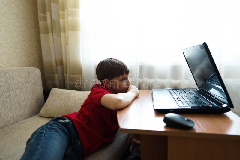 Der Junge liegt im Wohnzimmer auf der Couch und passt einen Film auf einem Laptop auf lizenzfreie stockfotografie Der Junge liegt im Wohnzimmer auf der Couch und passt einen Film auf einem Laptop auf lizenzfreie stockfotografie
