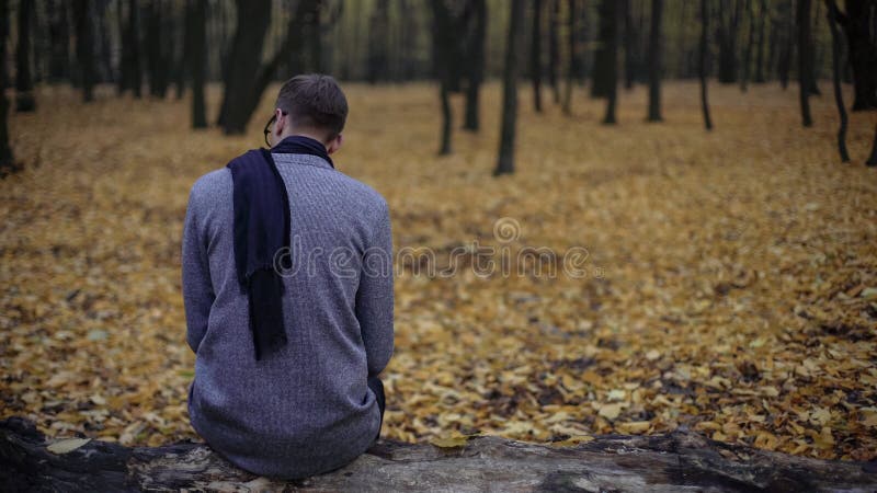 Der junge Mann, der allein im Herbstpark sitzt, glaubt Krise, Nostalgie, Einsamkeit