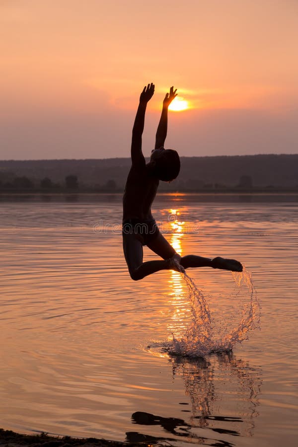 Der Junge springend in Wasser auf Sonnenuntergang lizenzfreies stockfoto Der Junge springend in Wasser auf Sonnenuntergang lizenzfreies stockfoto