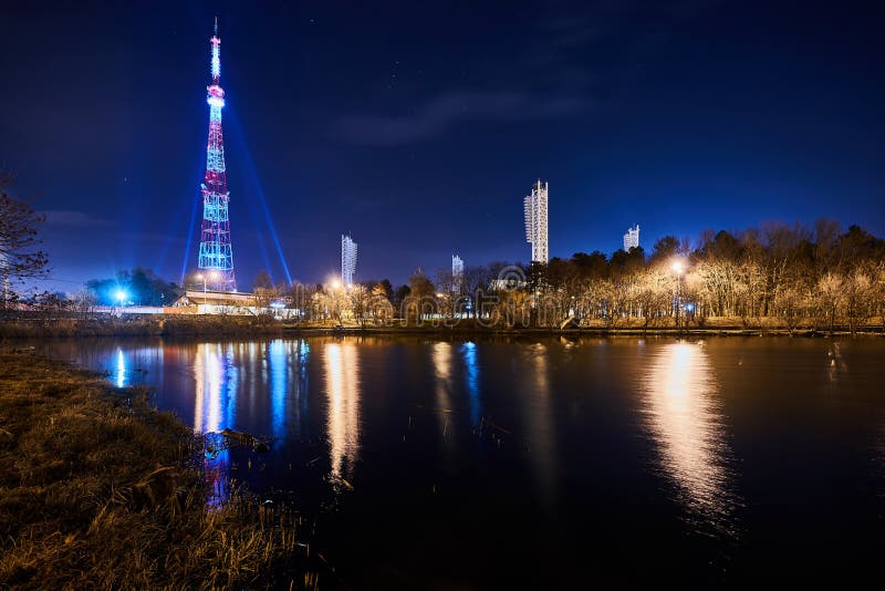 Krasnodar, Russia - December 9, 2018: The Krasnodar TV Tower and the Kuban Stadium at night, in the foreground is Lake Karasun, on average - a park. Krasnodar, Russia - December 9, 2018: The Krasnodar TV Tower and the Kuban Stadium at night, in the foreground is Lake Karasun, on average - a park