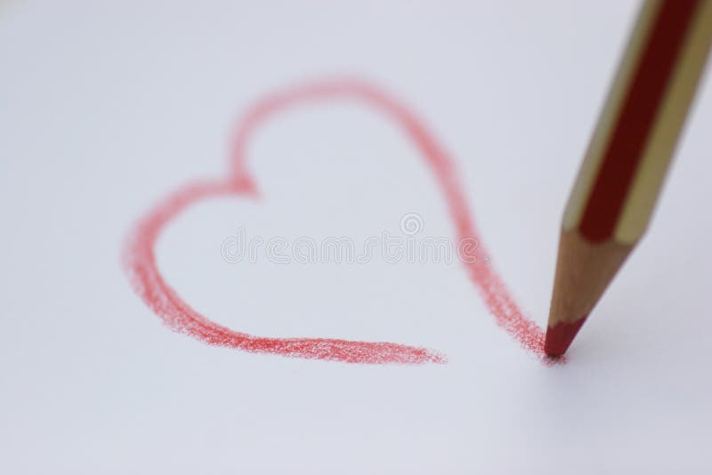 Red pencil drawing a heart on a white paper - focus is on the point of the pencil. Red pencil drawing a heart on a white paper - focus is on the point of the pencil.