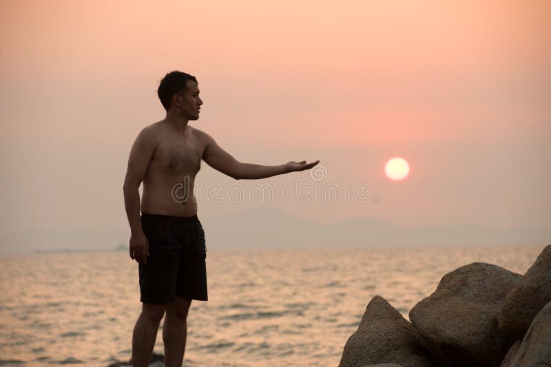 Male is engaged in fitness yoga exercise pointing the Sun on the stone in Sunset. Male is engaged in fitness yoga exercise pointing the Sun on the stone in Sunset.