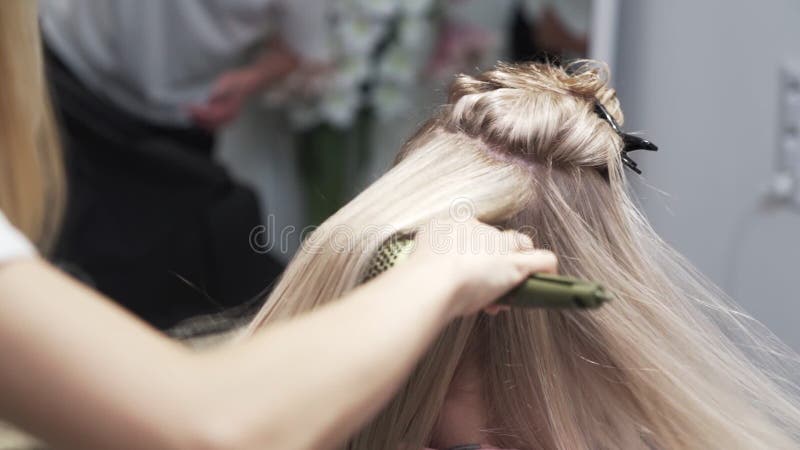 In der Nähe trocknet der Friseur lange blonde Frauenhaar mit Haartrockner und rundem Kamm.