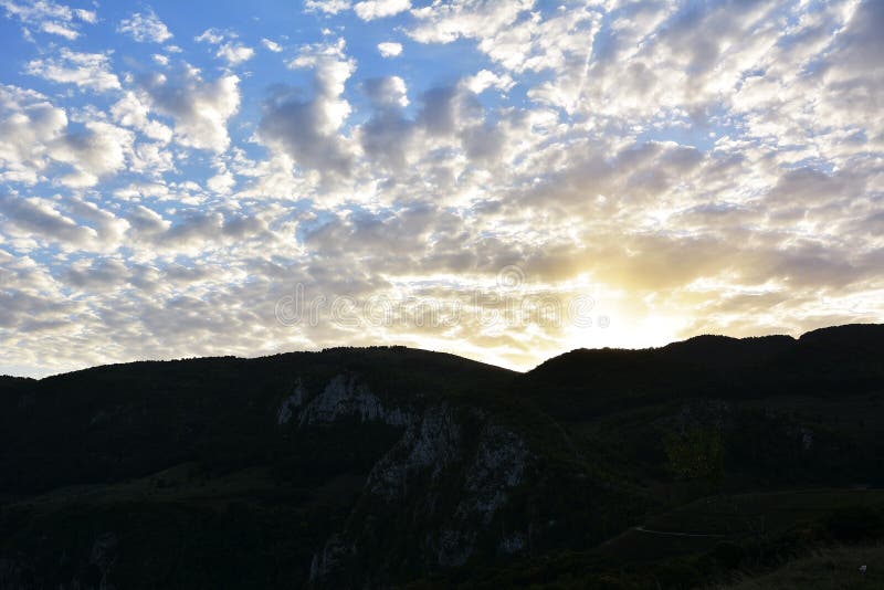 Der Sonnenuntergang hinter Berg mit schönem Sonnenstrahl durch die Wolke stockfotografie Der Sonnenuntergang hinter Berg mit schönem Sonnenstrahl durch die Wolke stockfotografie