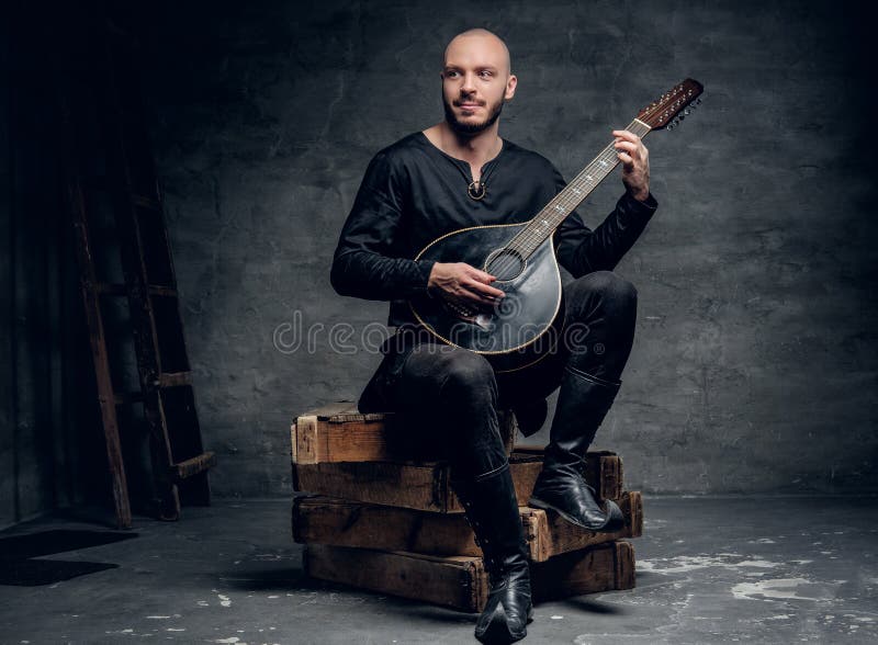 Der traditionelle Volksmusiker, der in der keltischen Kleidung der Weinlese gekleidet wird, sitzt auf einer Holzkiste und spielt stockbilder Der traditionelle Volksmusiker, der in der keltischen Kleidung der Weinlese gekleidet wird, sitzt auf einer Holzkiste und spielt stockbilder