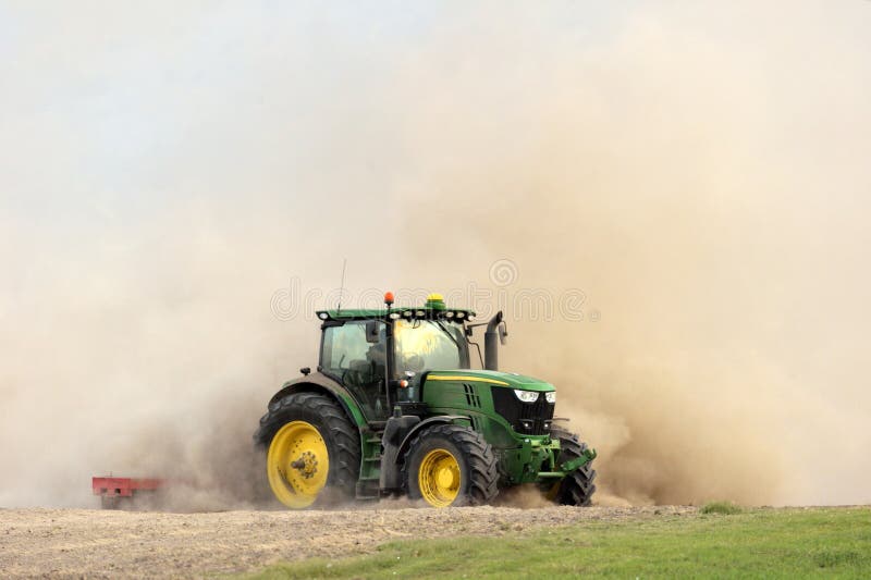 The tractor harrows the field in a huge dust cloud. Farmer in tractor preparing land for sowing. The tractor harrows the field in a huge dust cloud. Farmer in tractor preparing land for sowing.