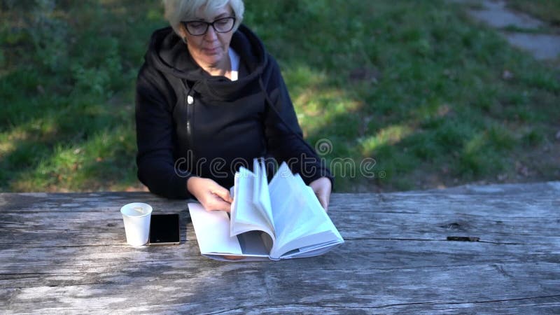 Der von mittlerem Alter sitzende Paginierung Frau durch ein Buch