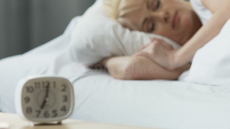 Der Wecker, der auf nightstand, die Frau schläft im Bett steht, trösten zu Hause