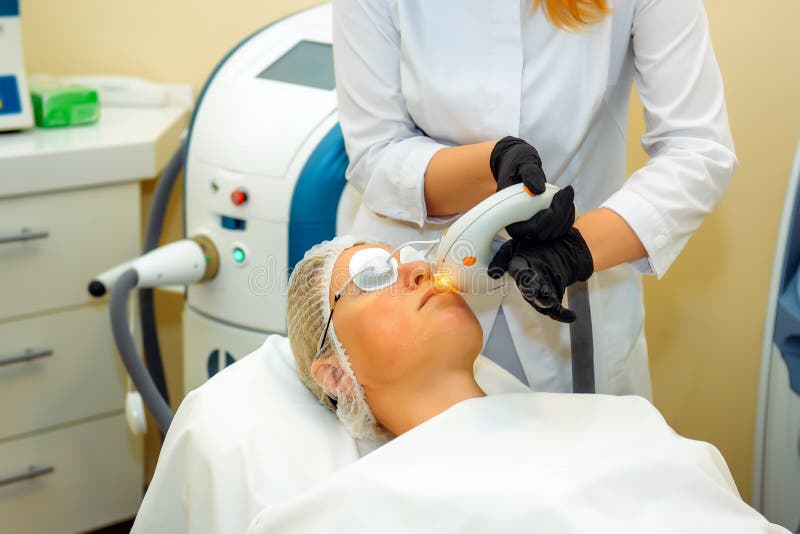 Dermatologist-cosmetologist with laser device makes facial rejuvenation procedure for a woman lying in the office of cosmetology royalty free stock photos Dermatologist-cosmetologist with laser device makes facial rejuvenation procedure for a woman lying in the office of cosmetology royalty free stock photos