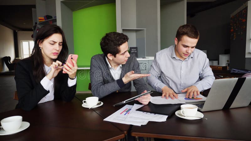 Educated and active colleagues, PC operators, two guys and girl do not cope with work and are nervous, quickly work for technology and with important documents, schedules and plans, rush to perform work and solve problems and issues, female uses mobile for negotiations, one of men`s busy In tablet and with papers, second guy uses computer, sitting to modern office during working hours. Man of European appearance with fair hair and short hair dressed in gray shirt, young men with short dark curly hair of European appearance dressed in white shirt and striped blue cardigan, European-looking women with long dark hair dressed in white blouse and black classic suit. Concept of successful and educated people, modern devices and technology, business and business, workload and exit from difficult situations, programming and work in IT field, education and science.r. Educated and active colleagues, PC operators, two guys and girl do not cope with work and are nervous, quickly work for technology and with important documents, schedules and plans, rush to perform work and solve problems and issues, female uses mobile for negotiations, one of men`s busy In tablet and with papers, second guy uses computer, sitting to modern office during working hours. Man of European appearance with fair hair and short hair dressed in gray shirt, young men with short dark curly hair of European appearance dressed in white shirt and striped blue cardigan, European-looking women with long dark hair dressed in white blouse and black classic suit. Concept of successful and educated people, modern devices and technology, business and business, workload and exit from difficult situations, programming and work in IT field, education and science.r