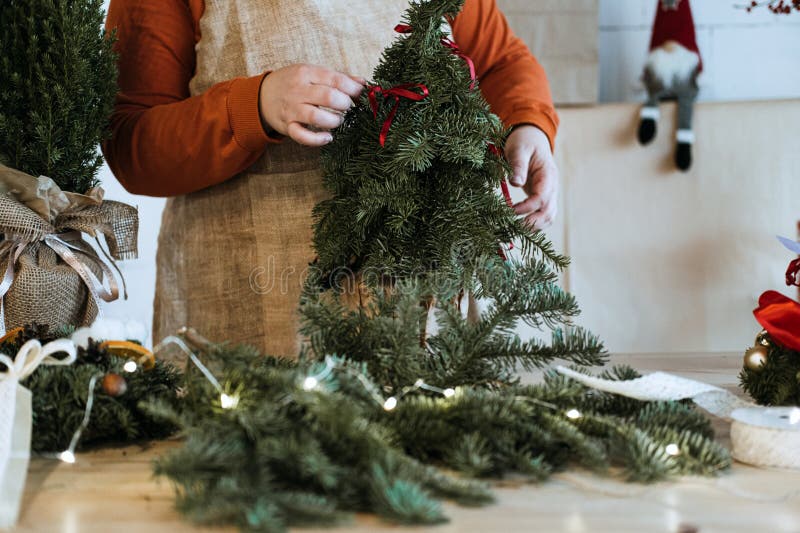 Des mains décorant un mini arbre de noël entouré de matériaux d'artisanat de vacances. présentation d'ateliers festifs et image libre de droits