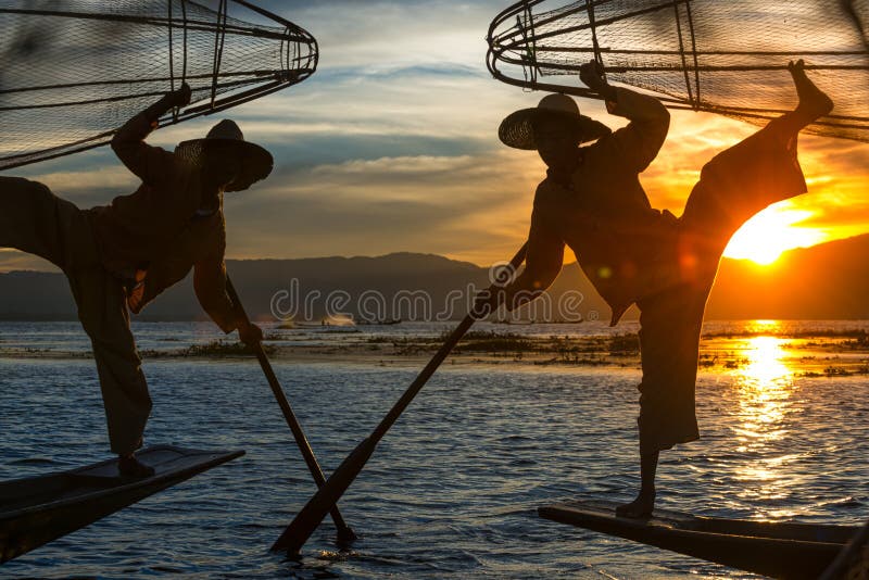 Des pêcheurs birmans posent avec des filets coniques au coucher du soleil, sur le lac Inle, dans la commune de Nyaungshwe, dans l image libre de droits Des pêcheurs birmans posent avec des filets coniques au coucher du soleil, sur le lac Inle, dans la commune de Nyaungshwe, dans l image libre de droits