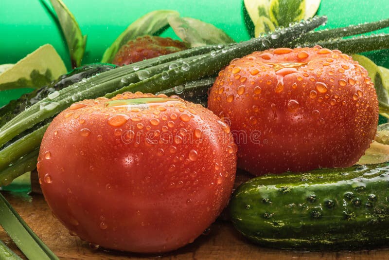 Des tomates rouges mûres, concombres verts, des plumes d'oignon vert sont couvertes de grandes gouttes de l'eau images stock Des tomates rouges mûres, concombres verts, des plumes d'oignon vert sont couvertes de grandes gouttes de l'eau images stock
