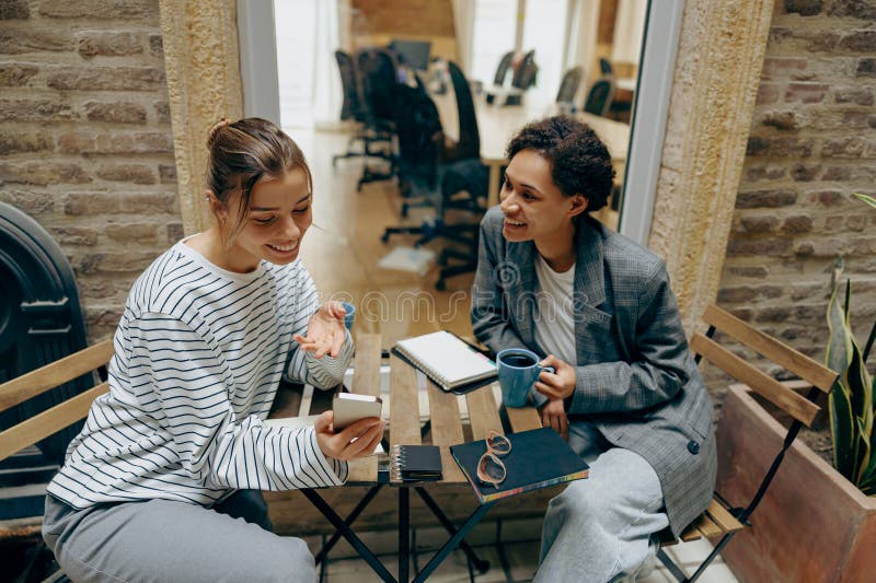 Two female colleagues have a coffee break time while sitting on office terrace. Two female colleagues have a coffee break time while sitting on office terrace