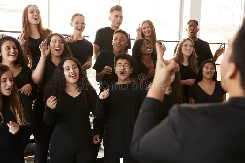 Male And Female Students Singing In Choir With Teacher At Performing Arts School. Male And Female Students Singing In Choir With Teacher At Performing Arts School