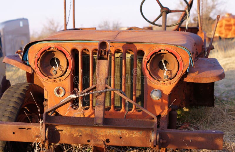 Old military jeep missing headlights and a wheel rusting in a field. Old military jeep missing headlights and a wheel rusting in a field