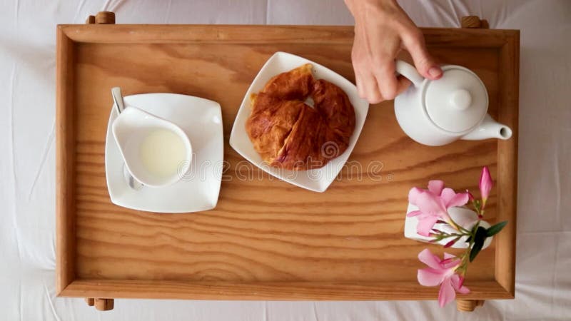 Desayuno en la cama las mujeres toman las manos vertiendo leche en una taza y tomando un trozo de croissant visto desde arriba