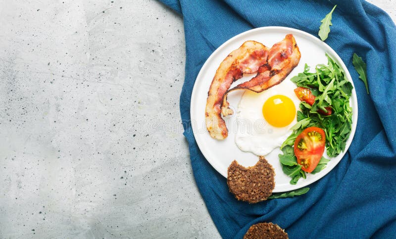 Desayuno ingl?s de alto valor proteico caluroso del estilo con el huevo, el tocino frito y el arugula en la placa Visi?n superior foto de archivo Desayuno ingl?s de alto valor proteico caluroso del estilo con el huevo, el tocino frito y el arugula en la placa Visi?n superior foto de archivo
