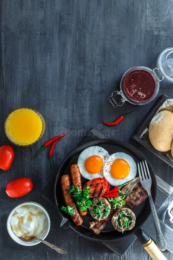 Desayuno inglés en una cacerola con los huevos fritos, las salchichas, el tocino, las setas, el atasco y el zumo de naranja en fo imagenes de archivo Desayuno inglés en una cacerola con los huevos fritos, las salchichas, el tocino, las setas, el atasco y el zumo de naranja en fo imagenes de archivo