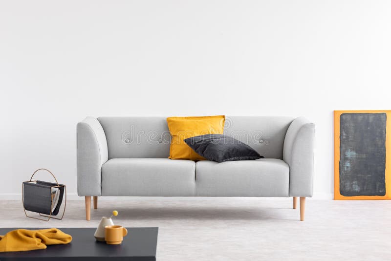 Descansos amarelos e pretos no canapé cinzento no interior espaçoso da sala de visitas com o quadro-negro na cremalheira alaranja imagem de stock Descansos amarelos e pretos no canapé cinzento no interior espaçoso da sala de visitas com o quadro-negro na cremalheira alaranja imagem de stock