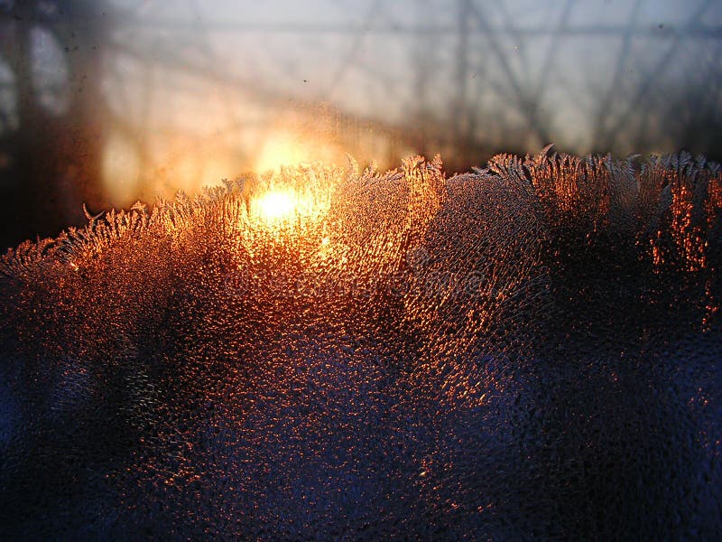 Descensos de los cristales y del agua de hielo de Frost en el vidrio de la ventana en el fondo de la salida del sol fotografía de archivo libre de regalías Descensos de los cristales y del agua de hielo de Frost en el vidrio de la ventana en el fondo de la salida del sol fotografía de archivo libre de regalías