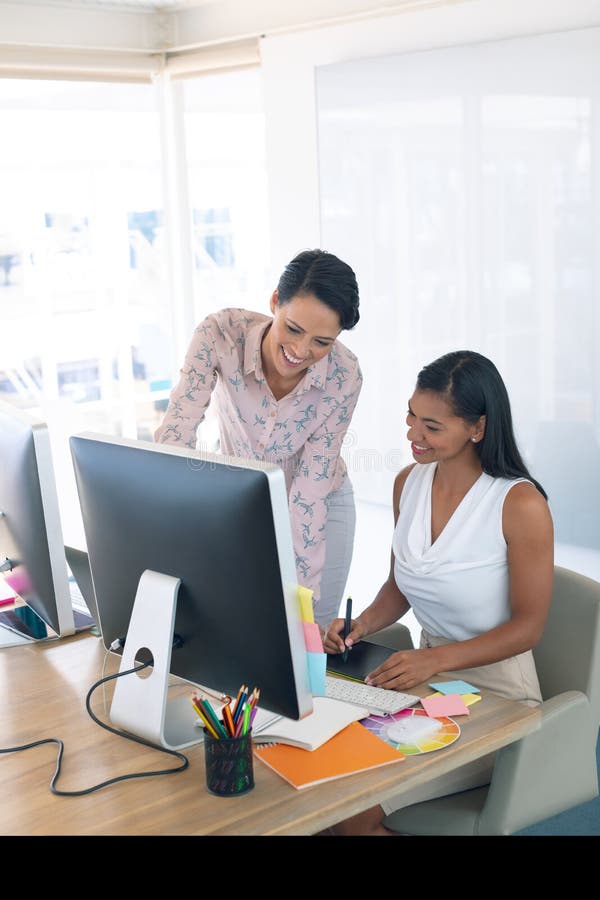 Designer gráficos fêmeas que discutem no computador na mesa em um escritório moderno foto de stock Designer gráficos fêmeas que discutem no computador na mesa em um escritório moderno foto de stock