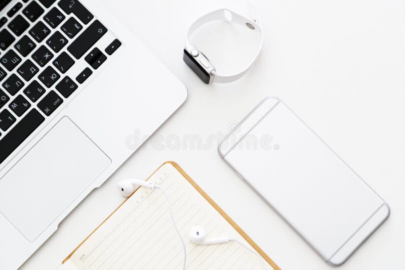 Desktop items: laptop, notebook, headphones, mobile phone, smart watch lying on white background. Flat lay, top view, overhead