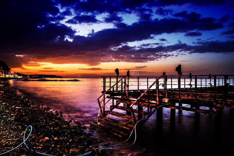 Una solitaria metallo costruito dock che ha usato allestito un aria di caffè e tè, casa al mare vicino al mare al tramonto con mare calmo e morbido cielo sullo sfondo.