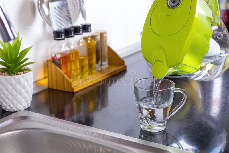 Pouring filtered water into glass from water filter jug in the kitchen. Purification and softening of drinking tap water. Closeup. Focus on glass. Pouring filtered water into glass from water filter jug in the kitchen. Purification and softening of drinking tap water. Closeup. Focus on glass