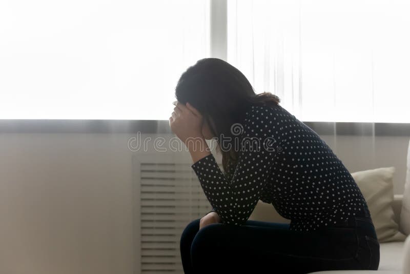 Desperate young woman sit on bed hiding face under palm having psychological problem difficult moment in life. Side shot of frustrated depressed female teenager lost in bad heavy thoughts. Copy space. Desperate young woman sit on bed hiding face under palm having psychological problem difficult moment in life. Side shot of frustrated depressed female teenager lost in bad heavy thoughts. Copy space