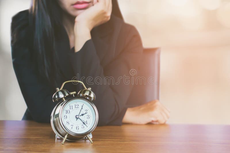 Desperdiçando o conceito do tempo com o sentimento asiático da mulher de negócio cansado e furado olhando o despertador na mesa foto de stock Desperdiçando o conceito do tempo com o sentimento asiático da mulher de negócio cansado e furado olhando o despertador na mesa foto de stock