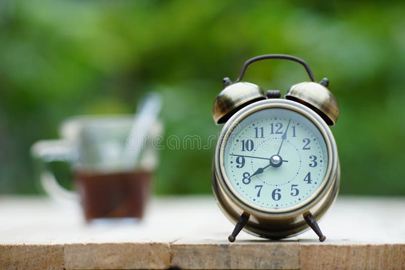 Despertador análogo na tabela de madeira com fundo do jardim do verde do borrão, 8 am , espaço da cópia imagens de stock Despertador análogo na tabela de madeira com fundo do jardim do verde do borrão, 8 am , espaço da cópia imagens de stock
