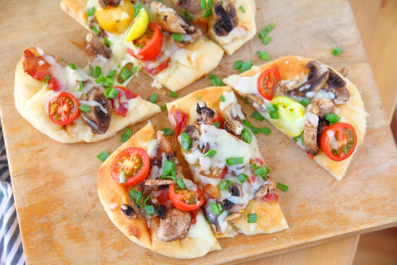 Naan pizzas with cherry tomatoes, mushrooms, bacon and scallions cut into portions. Naan pizzas with cherry tomatoes, mushrooms, bacon and scallions cut into portions