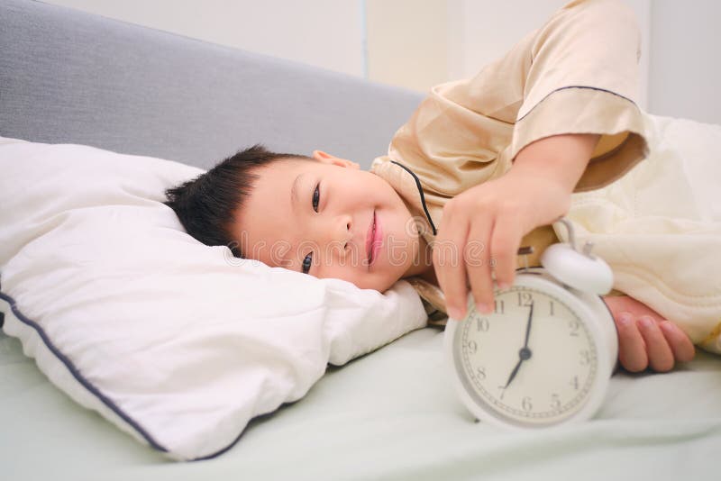 Despierta feliz niño pequeño y feliz en la cama y parando el despertador en el dormitorio en casa imagenes de archivo