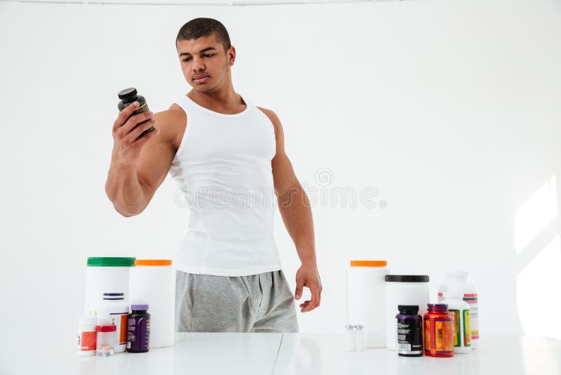 Desportista novo considerável perto da tabela com nutrição do esporte fotografia de stock Desportista novo considerável perto da tabela com nutrição do esporte fotografia de stock