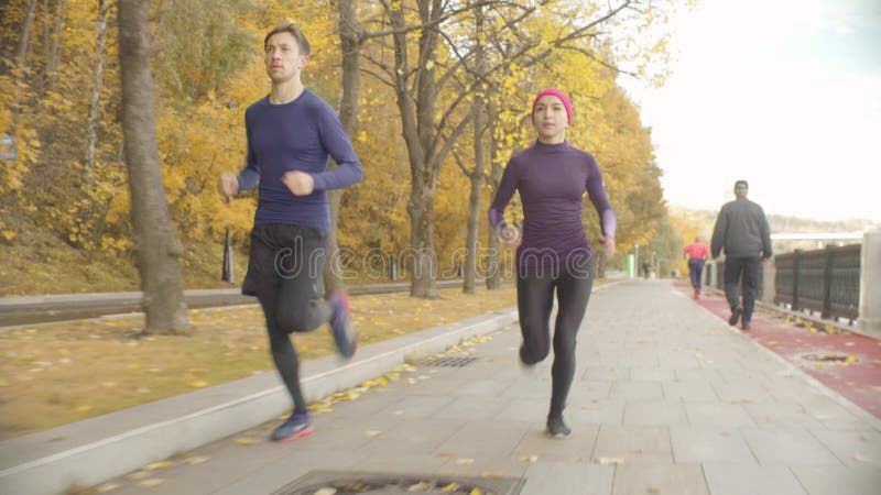 Desportista novo e desportista que correm ao longo da estrada