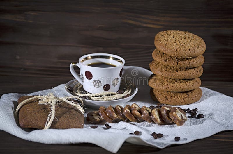 Dessert dolce con caffè, una pila di biscotti di farina d'avena e pan di zenzero su una tovaglia di tela bianca, fondo di legno, immagine stock libera da diritti Dessert dolce con caffè, una pila di biscotti di farina d'avena e pan di zenzero su una tovaglia di tela bianca, fondo di legno, immagine stock libera da diritti