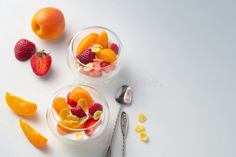 Dessert sain de vitamine légère de la fraise, de l'abricot et des cornflakes coupés en tranches avec de la crème dans des crémeuses en verre sur un fond blanc