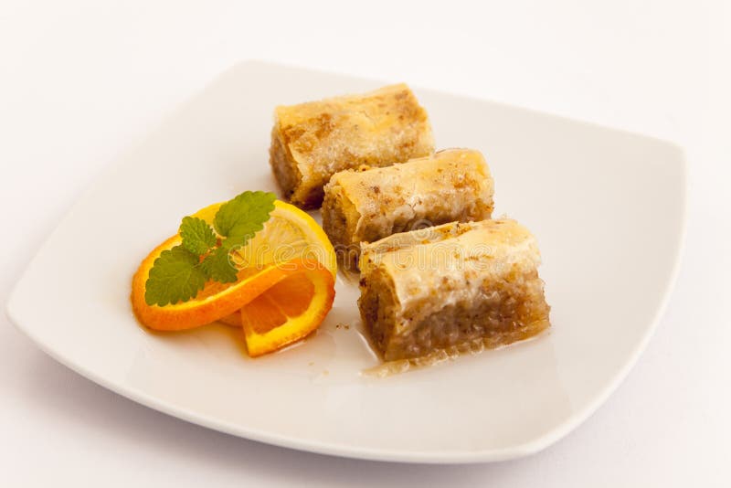 Tree Turkish baklava dessert on white plate with slice of orange. Tree Turkish baklava dessert on white plate with slice of orange