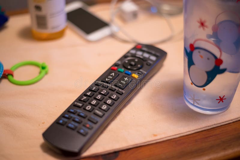 Dessus de table malpropre avec le verre à télécommande, d'eau, le téléphone, la boîte, le chargeur, et le jouet pour enfants photos stock Dessus de table malpropre avec le verre à télécommande, d'eau, le téléphone, la boîte, le chargeur, et le jouet pour enfants photos stock